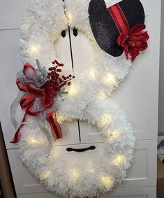 a white wreath with red bows and lights hanging on the front door to decorate it