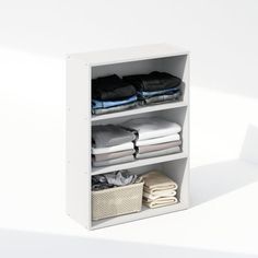 an open white shelf with folded clothes and baskets on the bottom, against a white background