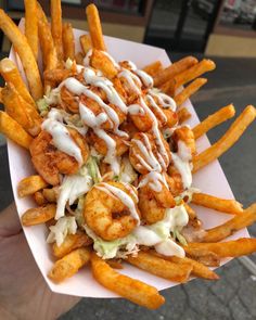 a person holding a plate full of french fries covered in sauce and toppings on it