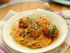 a white bowl filled with spaghetti and meatballs on top of a table next to a fork