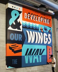 a man is standing in front of a large sign that says, we are developing our wings and the way