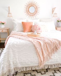 a white bed with pink pillows and blankets on top of it, along with a round mirror above the headboard