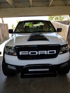 the front end of a white truck parked in a parking garage next to a wooden fence