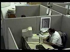 an office cubicle with a man sitting at a desk in front of a computer monitor