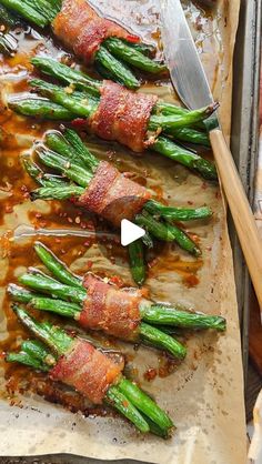 asparagus wrapped in bacon and sitting on a baking sheet with a spatula