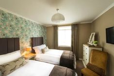 two beds in a hotel room with green wallpaper and brown headboards on either side of the bed