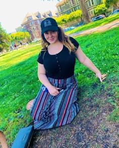 a woman sitting on the ground with a suitcase and hat in her hand, next to a tree