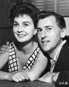 an old black and white photo of a man and woman sitting at a table with their arms around each other