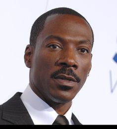 a close up of a person wearing a suit and tie with a moustache