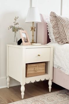 a white nightstand with a basket on it next to a bed