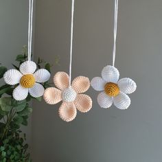 three crocheted flowers hanging from strings next to a potted plant and wall