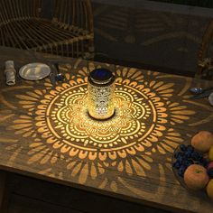 a wooden table topped with fruit and a lit candle on top of it next to two wicker chairs