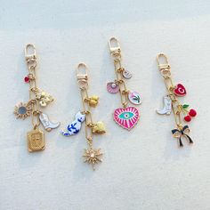 four key chains with charms attached to them on a white surface, one has an umbrella and the other is a suitcase