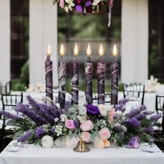 a table topped with lots of purple and white flowers next to tall black candle holders