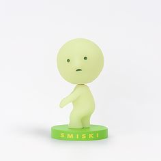 a small plastic figure is standing on a green base with the word smiski written below it