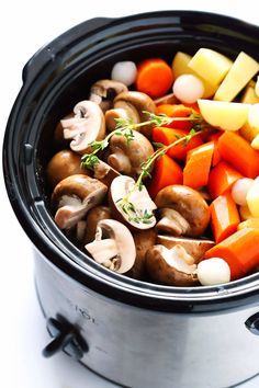 a crock pot filled with mushrooms, carrots and potatoes