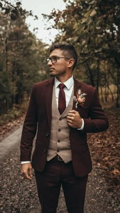 a man in a suit and tie standing on a dirt road with trees behind him