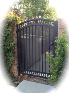 an iron gate in front of a stone wall with vines growing on it and a concrete slab below