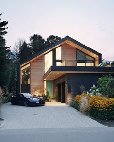 a car is parked in front of a house with large windows and wooden sidings