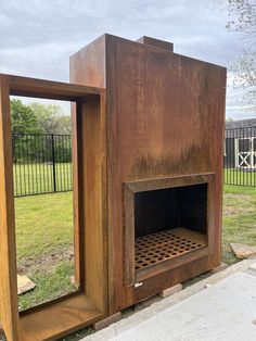 an outdoor fireplace made out of wood in the middle of a park with grass and trees