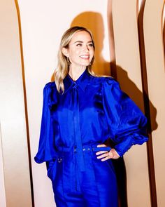 a woman standing in front of a wall wearing a blue shirt and pants