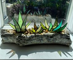 three green glass plants sitting on top of a piece of driftwood in front of a window