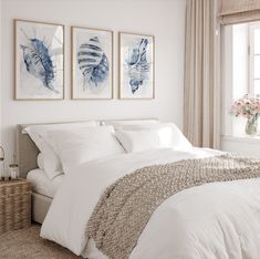 a bed with white sheets and pillows in a bedroom next to two paintings on the wall