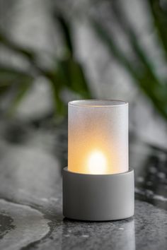 a small white candle sitting on top of a table next to a potted plant