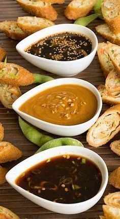 several small bowls filled with dipping sauce next to bread rolls on a wooden table top