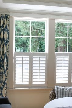 a living room filled with furniture and two large windows covered in white shuttered blinds