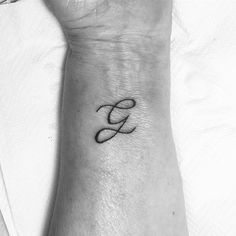 a black and white photo of a wrist tattoo with the letter g in cursive font