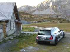 a car is parked in front of an old wooden house with mountains in the background