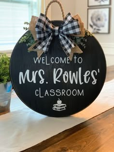 a welcome sign with a bow hanging from it's center piece on top of a table