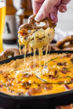 bacon and beer cheese dip is being lifted from a skillet with a pretzel in it