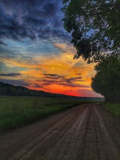 the sun is setting over a dirt road