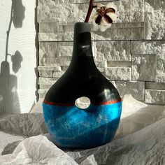 a blue and black vase sitting in front of a brick wall with a flower sticking out of it