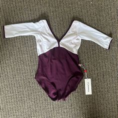 a purple and white one piece swimsuit laying on the floor next to a tag