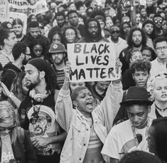 a large group of people holding signs and standing in front of a crowd with black lives matter written on them