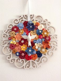 a clock made out of paper flowers on a white wall with an ornament hanging from it