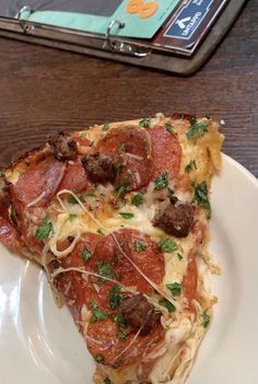 a slice of pizza on a white plate sitting on a table next to a magazine