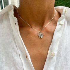 a woman wearing a white shirt with a flower necklace on her neck and button buttons