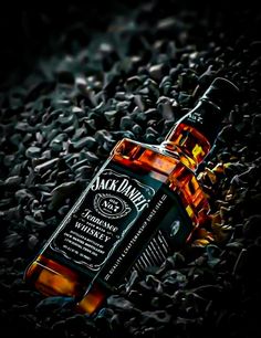 a bottle of jack daniels whiskey sitting on top of some rocks and gravel in the dark