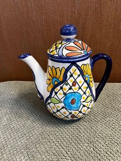 a ceramic teapot with a painted design on the top and bottom, sitting on a table