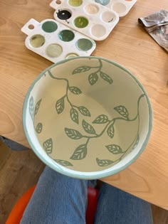 a person sitting at a table holding a bowl with leaves painted on it