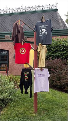 several shirts hanging on a clothes line in front of a building with grass and bushes