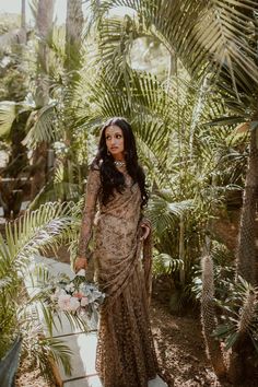 a woman standing in front of palm trees wearing a long dress and holding a bouquet