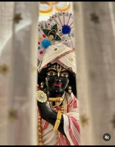 a statue is dressed in black and white with colorful decorations on its head, surrounded by curtains