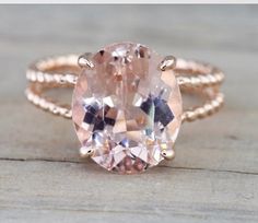 an oval shaped morganite sits on top of a wooden surface, surrounded by two gold rings