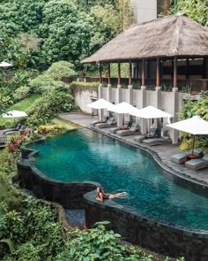 a woman laying on the edge of a pool next to an umbrella covered area with lounge chairs