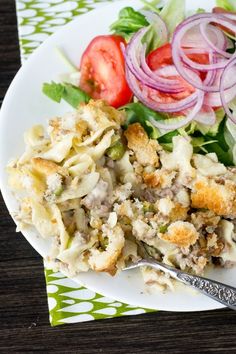 a white plate topped with pasta and salad next to a fork on top of a table